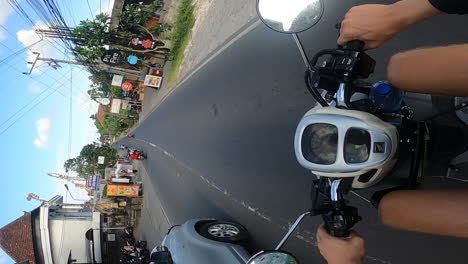 Vertical-shot-of-biker-driving-through-streets-of-Canggu-during-day,-Bali