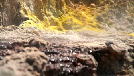 Mineral-liquid-flowing-on-rocks-with-yellow-sulfur-in-background,-focus-pull
