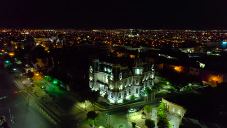 Aerial-view-away-from-the-Illuminated-Quinta-Gameros-building-in-Chihuahua,-night-in-Mexico---pull-back,-drone-shot