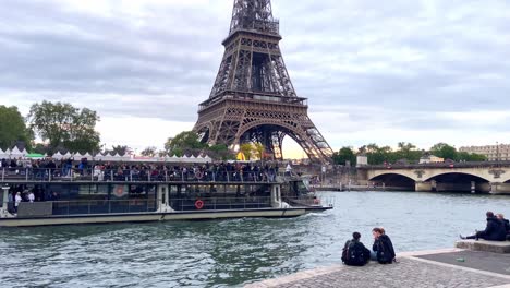 Tourists-Ride-On-An-Open-Excursion-Boat-Cruising-In-The-Seine-With-Eiffel-Tower-And-Pont-d'Lena-In-Paris,-France
