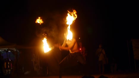 Asian-male-spinning-fire-with-throw-and-catch-creating-large-fireball-visual,-filmed-in-handheld-style