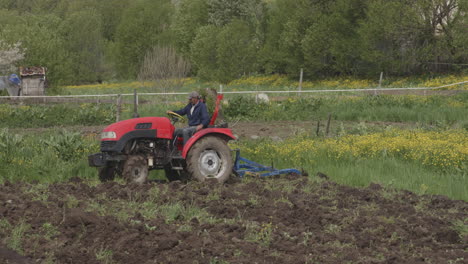 Farmer-Driving-Red-Tractor-Plowing-Agricultural-Farm-Field-In-Moliti-Village,-Georgia
