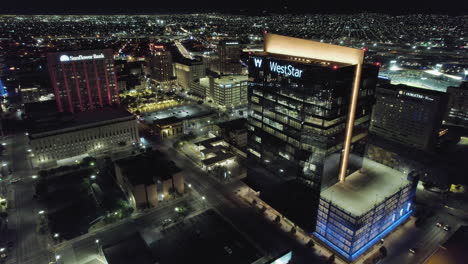 Vista-Aérea-De-Drones-Del-Centro-De-El-Paso-Texas-Durante-La-Noche-Con-El-Edificio-Del-Banco-Weststar-En-Primer-Plano-Y-Las-Luces-De-La-Ciudad-En-Segundo-Plano