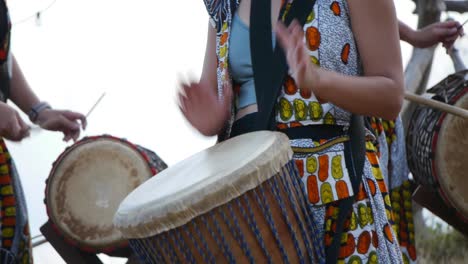 Asian-women-playing-percussive-African-drum-instruments-with-drum-sticks-and-hands,-filmed-in-handheld-style-as-tight-medium-shot