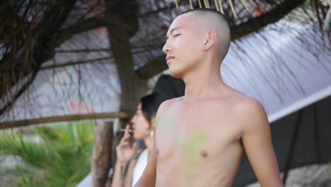 Asian-man-with-shaven-head-dancing-rhythmically-at-outdoor-music-festival-while-holding-can,-filmed-in-handheld-style-as-tight-medium-shot