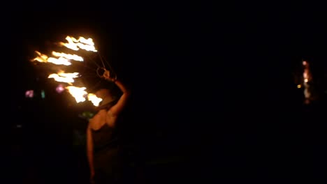 Asian-woman-spinning-and-rotating-single-fire-fan-in-right-hand-during-night,-filmed-in-handheld-style
