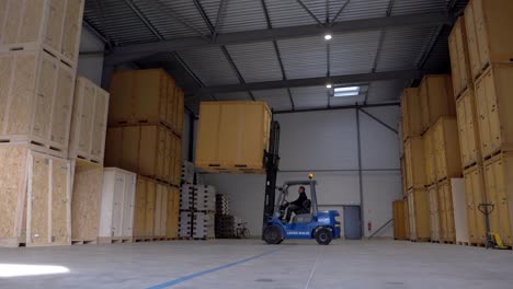 Worker-in-forklift-transporting-large-box-in-industrial-warehouse,-wide-shot