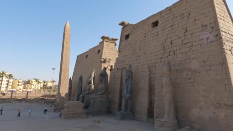 Temple-of-Luxor-entrance,-statues-of-Ramses-II-and-Pylon,-tourists-enter-the-temple-in-Egypt