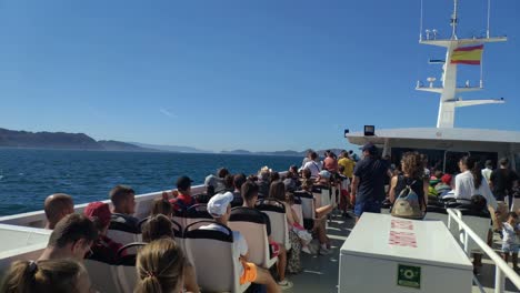 passengers-sitting-on-the-deck-of-the-ship-sailing-to-the-islands-Cíes,-Rías-Baixas,-Spanish-flag-and-antennas-in-the-captain's-cabin,-day-out-and-sunny,-shot-turning-left,-Pontevedra,-Galicia,-Spain