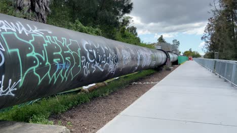 Big-pipe-crossing-with-graffiti-spray-painting-vandalism-next-to-Cooks-River-at-the-Airport-Drive,-Mascot-Sydney,-New-South-Wales