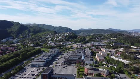 Asane-district-with-mall-besides-church-and-sports-hall-outside-Bergen-Norway---Urban-aerial-at-sunny-summer-day-with-highway-passing-in-left-frame