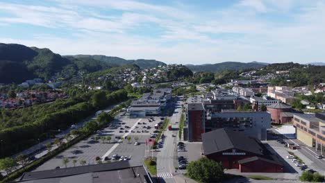 Ascending-aerial-from-Asane-district-outside-Bergen-during-summer-morning---Sports-hall-and-church-seen-besides-shopping-mall-and-road-before-revealing-distant-mountain-landscape