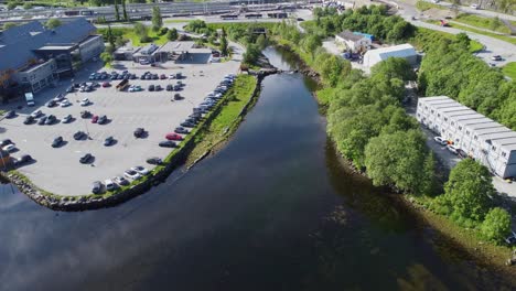 Arna-salmon-river-outside-Bergen-during-summer---Birdseye-aerial-looking-down-at-glassy-water-surface-of-river-close-to-parking-lot-and-urban-area