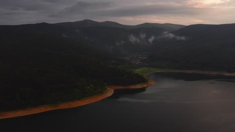 Aerial-view-of-mountains-surrounding-a-gorgeous-lake-with-a-small-town-on-it's-banks-during-sunset