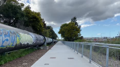 Concrete-pedestrian-walking-path-with-fence-and-big-pipe-with-unique-spray-paint-graffiti