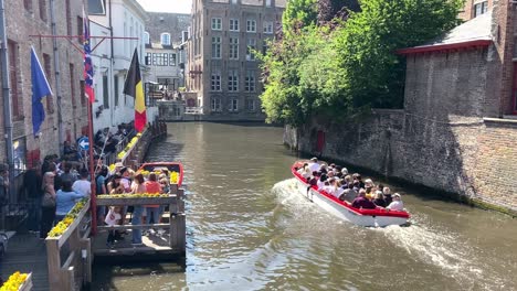 Speedboat-With-Passengers-Cruising-In-The-City-Canal-Passing-By-Tourists-Waiting-On-The-Terminal-In-Bruges,-Belgium