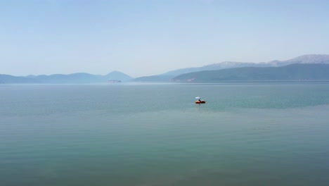Man-relaxing-in-his-small-boat-on-blue-Lake-Prespa-on-a-sunny-nice-day-with-mountains-in-the-background
