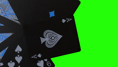Birdeye-Rotierende-Aufnahme-Von-Schwarzen,-Stilvollen-Casino-Pokerkarten-Mit-Blauer-Farbe-Im-Inneren-Neben-Einem-Greenscreen