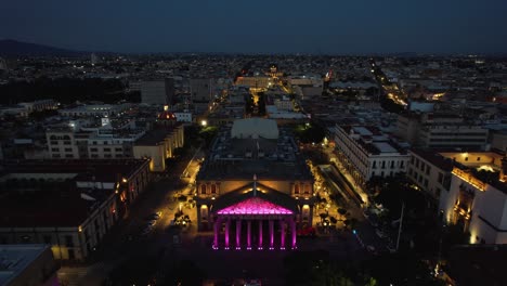 Aerial-view-over-the-colorful-lit-Teatro-Degollado,-dusk-in-Guadalajara,-Mexico---reverse,-drone-shot