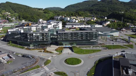 Distant-aerial-approaching-Horisont-shopping-mall-and-apartment-building-in-Asane-outisde-Bergen-Norway---Sunny-summer-day-aerial-moving-towards-building-above-road
