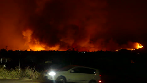 Large-forest-fire-in-California-at-night-and-car-passing-in-foreground