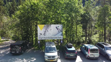High-rope-and-zipline-park-by-Voss-Active-in-Voss-Norway---Aerial-moving-towards-billboard-sign-at-parking-lot