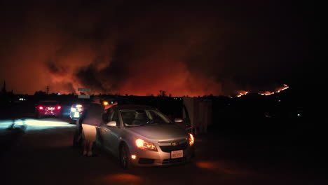 Gente-En-Coche-Por-La-Noche-Frente-Al-Cielo-Naranja-Por-Incendios-Forestales,-California