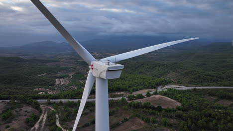 Close-up-aerial-view-orbiting-stationary-wind-turbine-on-overcast-Barcelona-mountain-range-farmland