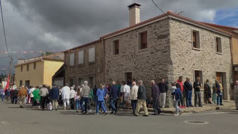 Catholic-religious-people-leave-the-church-in-procession-delnate-of-a-stone-house-in-celebration-under-the-control-of-the-police,-cloudy-day,-blocked-shot,-Poulo,-A-Coruña,-Galicia,-Spain