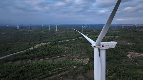Close-up-aerial-view-passing-Barcelona-renewable-wind-turbines-rotating-on-agricultural-farmland