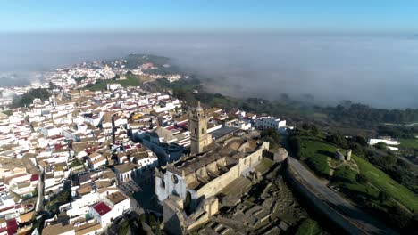 Aerial-drone-shot-over-medina-sidonia-in-andalucia-spain-with-focus-on-the-church-of-santa-maria-with-view-of-the-old-town-and-clouds-on-a-sunny-day