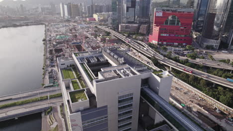 Aerial-drone-backward-moving-shot-over-roof-electromechanical-equipment-of-Hong-Kong-Children's-Hospital,-China-with-heavy-traffic-movement-in-the-background-at-sunset