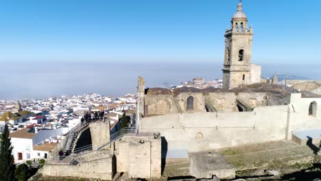 Aerial-dolly-shot-of-the-church-of-santa-maria-in-medina-sidonia-in-andalucia-in-spain-overlooking-the-historic-old-town-with-white-buildings-on-a-cloudless-summer-day