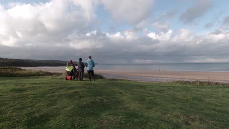 Hiking-family-support-pensioner-in-wheelchair-looking-away-across-stormy-coastal-horizon