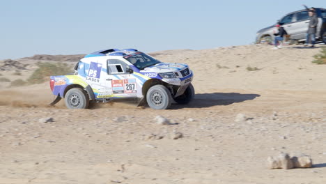 Coche-De-Rally-Conduciendo-Rápido-Por-La-Pista-De-Tierra,-Arrojando-Polvo-Al-Aire-En-Dakar-En-Arabia-Saudita