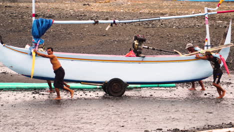People-pushing-heavy-indonesian-fishing-boat-towards-ocean-water,-side-view