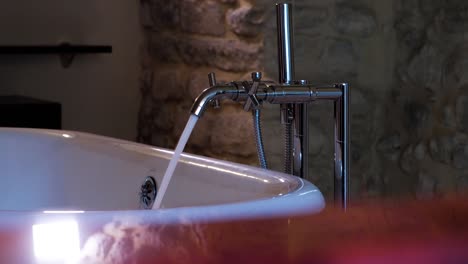 Slow-motion-shot-of-a-bath-tap-filling-the-tub-in-a-stone-bathroom