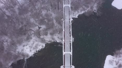 Top-down-aerial-view-of-a-bridge-crossing-a-river-with-snow-actively-falling