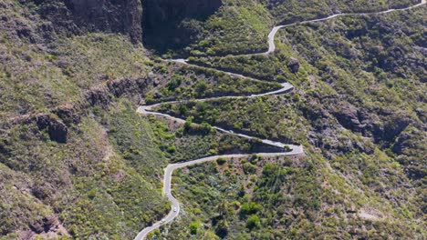 Steep-mountain-road-going-up-green-slope-on-Tenerife,-Canary-Island,-aerial