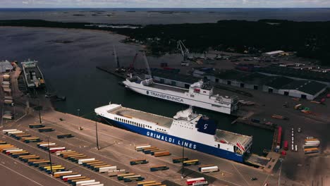 Aerial-view-of-cargo-ships-at-a-shipping-terminal,-summer-in-Hanko,-Finland---reverse,-tilt,-drone-shot