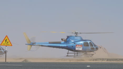 Dakar-helicopter-take-off-from-sandy-desert-roadside-as-cars-pass-through-dust