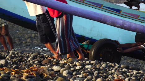 Indonesian-fishermen-pulling-heavy-boat-out-of-ocean-water,-Bali-island