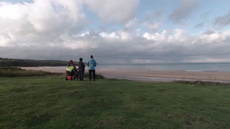 Family-supporting-pensioner-grandmother-in-wheelchair-watching-overcast-sandy-beach