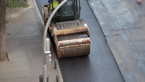 View-from-above-of-a-double-drum-road-roller-machine-while-compacting-recently-layed-tarmac-on-city-streets