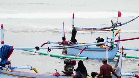 Pan-shot-and-zoom-in-of-fishermen-putting-typical-Indonesian-canoe-in-sea,-Bali