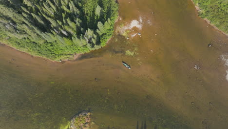 High-flying-drone-shot-looking-down-over-a-small-canoe-drifting-down-a-river