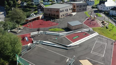 Playground-and-tilt-up-to-reveal-Vaksdal-elementary-school-building-in-Norway---Aerial-with-kids-playing-outside