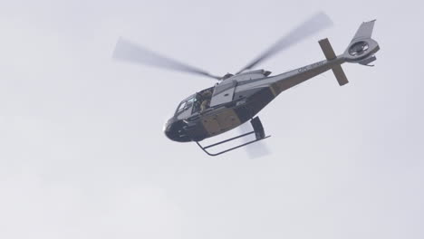 Low-Angle-View-of-Military-Helicopter-With-Solder-on-Door-Flying-Under-Cloudy-Sky,-Tracking-Shot