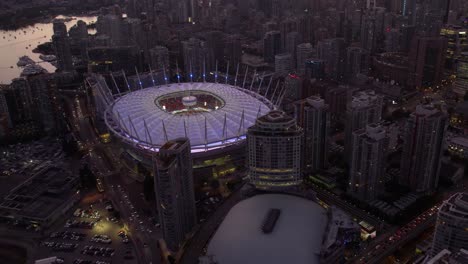 Aerial-view-overlooking-the-illuminated-BC-Place-Stadium-and-Rogers-place-arena,-evening-in-Vancouver,-Canada---reverse,-drone-shot
