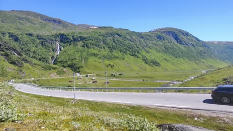 Cars-climbing-Halsabakkane-hills-towards-mountain-Vikafjell-at-road-rv-13-in-Norway---Beautiful-lush-green-meadow-and-farmland-in-mountain-landscape-background---Handheld-static-clip-Norway